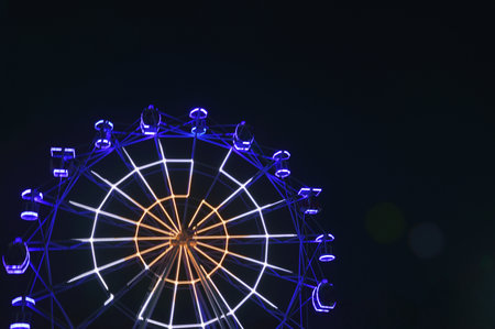 The Ferris wheel glows blue against the night sky. Rides in the park.