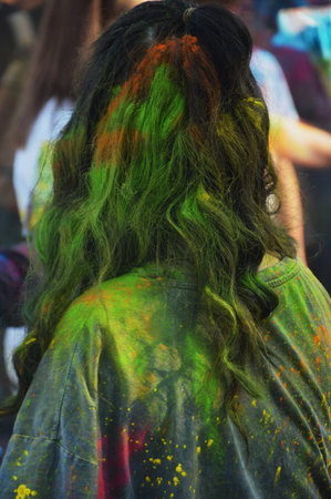Bright colored spots of powder green paint on hair and clothes of teenager, young girl. Street festival of colors.の写真素材