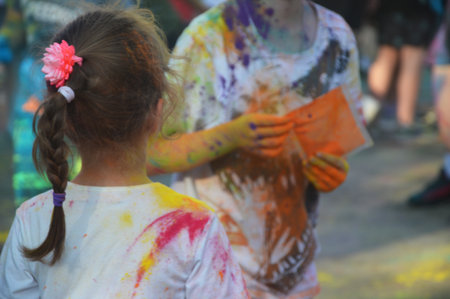 Children in clothes with multi-colored paint stains. Festival of colors on the street.