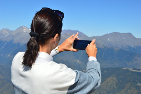 Brunette woman stands with her back and takes a photo of a beautiful mountain landscape on her...