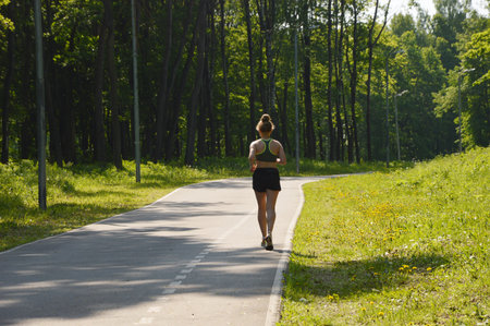 A woman in black shorts and a top runs along a forest sports track.