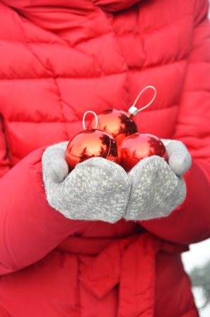 Female hands in gray knitted mittens hold red shiny balls. Christmas Eve.の写真素材