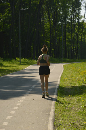 Woman in sports top and shorts jogging on road. Rear view.の写真素材