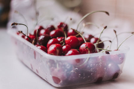 Ripe washed cherry in a container on a white table, fresh harvestの写真素材