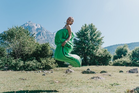 the girl in the sleeping bag, jumping on a background of mountainsの写真素材