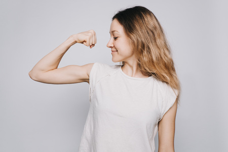 confident young sporty Caucasian woman in a white t-shirt showing biceps against white backgroundの写真素材