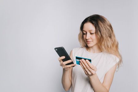 young beautiful Caucasian girl in a white t-shirt makes a purchase using a mobile phone and credit...