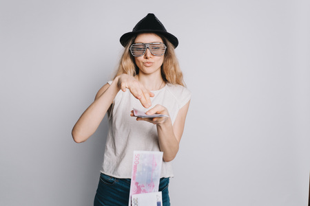 Young attractive confident girl in glasses and a hat spends Euro banknotes on a white background. Easy to part with money.の写真素材