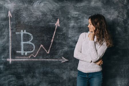 Girl watching the chart of bitcoin exchange rate drawn on black chalkboard with chalkの写真素材