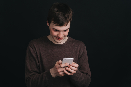 A man looks at a mobile phone screen and dials the message , the portrait of a man close up in Studio on dark backgroundの写真素材