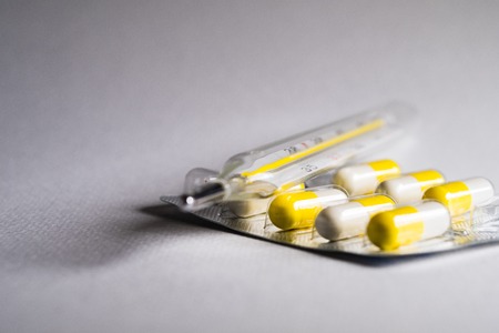 Thermometer and pills on a white gray background. Influenza and seasonal illnesses, copy space.