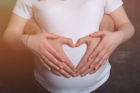 Parents make a heart on the belly of a pregnant mother against a dark background, toningの写真素材