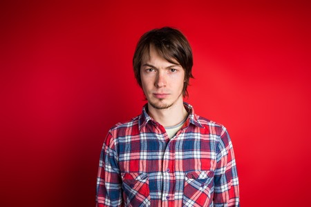 The man looks at the camera sternly. Portrait of a man in a red checkered shirt on a red background, close-up.の写真素材