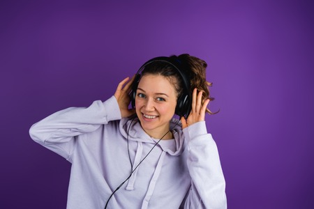 Beautiful girl listening to music wearing headphones in a sweatshirt on a purple backgroundの写真素材
