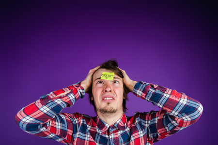 Caucasian man looks at a sticker with the inscription credit, grabs his head, close-up portrait. The man is shocked by the interest on the loan - the purple backgroundの写真素材
