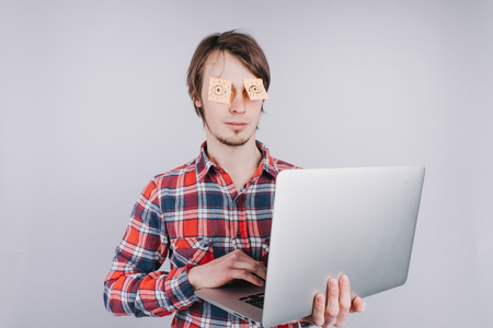 Man prints on a computer with his eyes closed, stickers with painted eyes are glued to the eyes of a guy, an isolated white backgroundの写真素材