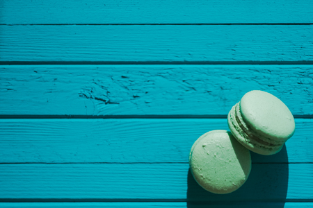 Two green macaron or macaroons on a turquoise wooden background, almond cookies in pastel tones, top view, copy spaceの写真素材