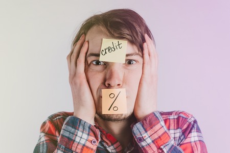 Stickers with the inscription credit and interest are glued on the forehead of the man and the mouth - the guy grabs his head with his hands, the concept of loans and debts, tonedの写真素材
