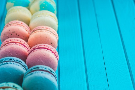 Multicolored macaroons lie in a row on a turquoise wooden background, almond cookies in pastel tones, copy spaceの写真素材