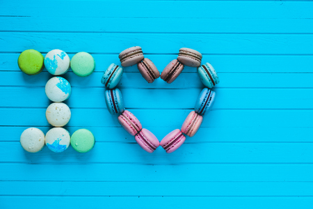 I love - multicolored macaroons in the form of hearts and confessions of lovers lie on a turquoise wooden background, copy spaceの写真素材