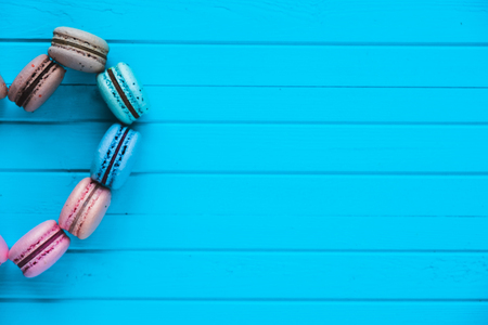 Multicolored macaroons in the form of a half heart lay on a turquoise wooden background, copy spaceの写真素材