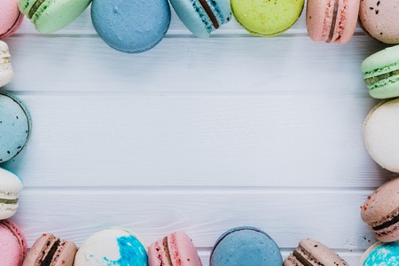 Multicolored frame from macaroons or macaron on a white wooden background, almond cookies in the form of decoration, copy spaceの写真素材