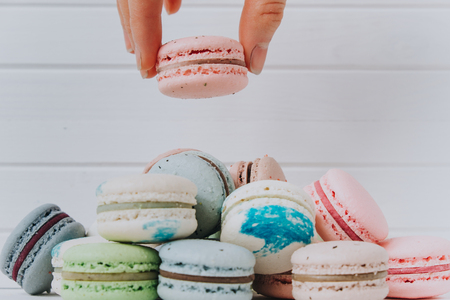 Female hand puts macaroons in a pile of almond cookies on a white wooden background, copy spaceの写真素材