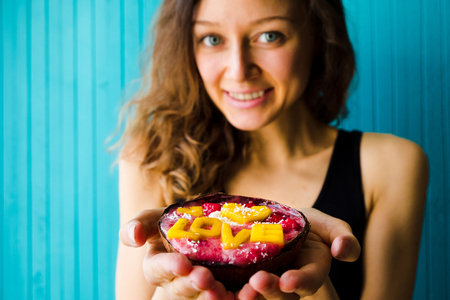 Smiling young woman holding a smoothie bowl on a turquoise wooden background, copy space. The concept of proper nutrition and healthの写真素材