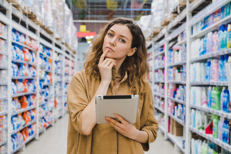 Business woman is thinking about shopping with a tablet in hand in a supermarketの写真素材