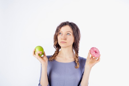 Beautiful girl is holding an apple and a donut in her hands. Concept of a healthy diet and dietの写真素材