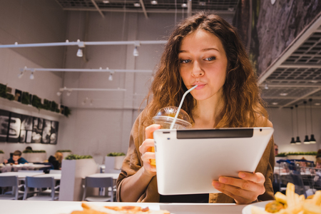 Business woman looking at a tablet and drinking juice from a tube in a fast food cafeの写真素材