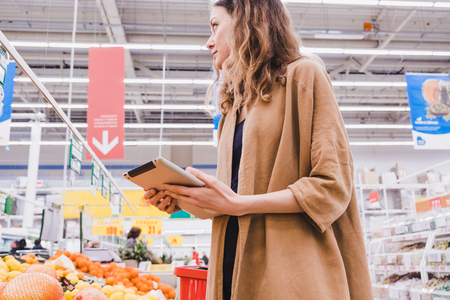 Young business woman with a tablet in her hands buys food in a supermarketの写真素材