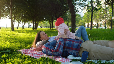 Happy family lies on the grass and plays with the child at sunset in the parkの写真素材