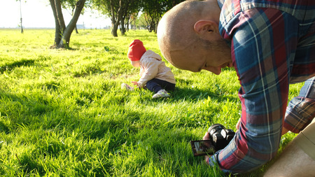 Young father taking pictures of daughter in the park at sunset.の写真素材