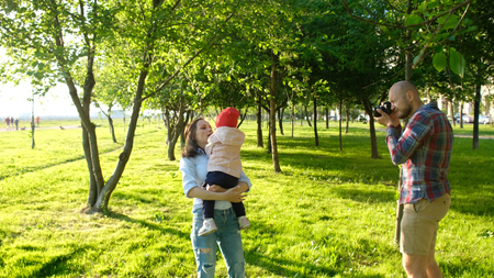 Young father taking pictures of mother and daughter playing in the park at sunset. Happy family having a rest and photographed on the natureの写真素材