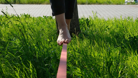 Woman legs walk along a tight line in the park. Foot woman balances on the slackline close up