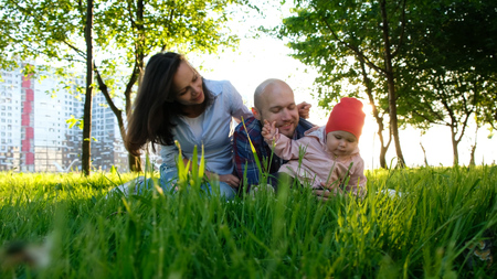 Happy family is resting on nature. Parents play with a small baby daughter in a park in the summer at sunset, camera movementの写真素材