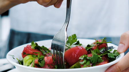 Woman eats raw fork salad of cucumbers and tomatoes with greens in a restaurant close-up.の写真素材