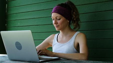 Smiling business woman tourist freelancer typing on a laptop outdoors in summer against a green wallの写真素材