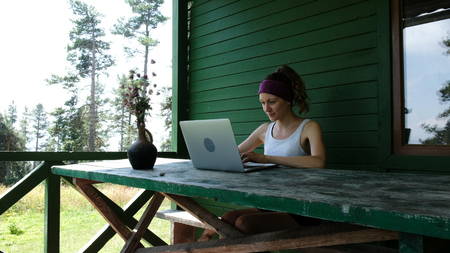 Smiling business woman tourist freelancer typing on a laptop outdoors in summer against a green wall at a recreation center in the forestの写真素材