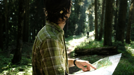 Man tourist standing in the forest and checks the route on a paper map and looks at the pathの写真素材