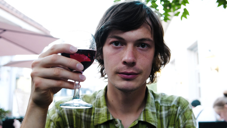 Man on a date raises a glass of wine and clink glasses. Guy in love smiles in a restaurant at dinnerの写真素材