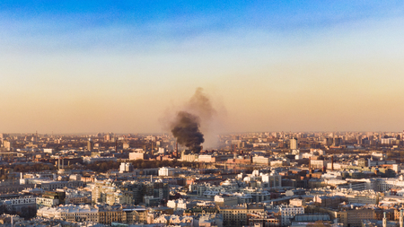 Fire in the city, a column of black smoke rises above horizon, aerial viewの写真素材