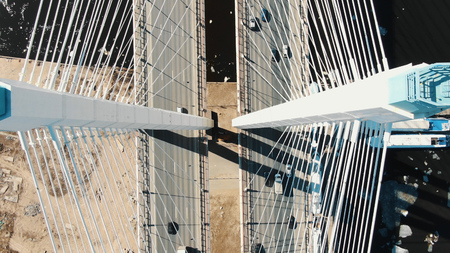 Drone take off up along the cable-stayed bridge supports. On bridge go streams of trucks and cars.