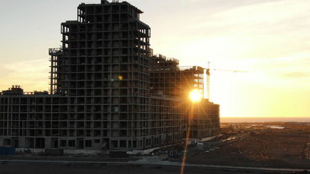 Shooting from a drone under construction residential building with construction cranes at sunset, the drone flies up to the construction siteの写真素材