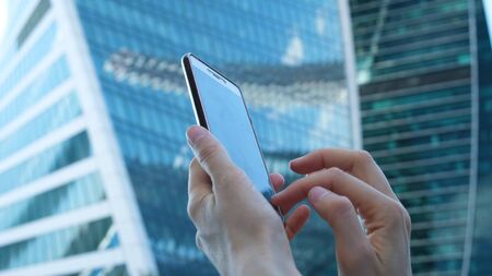 female hands are using a smartphone against the background of large glass business centers, close-upの写真素材