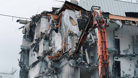 Excavator destroys the old building. Demolition work, pieces of concrete and reinforcement fall downの写真素材