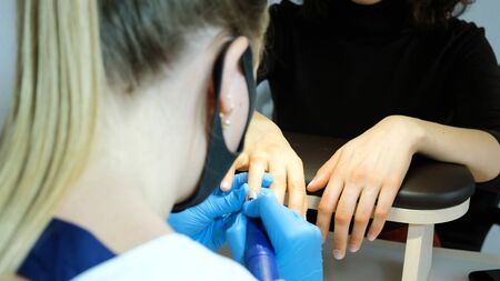 Manicurist, nail artist handles nails with manicure milling cutter. Beauty service, nail salon, health care and cosmetics. Close upの写真素材