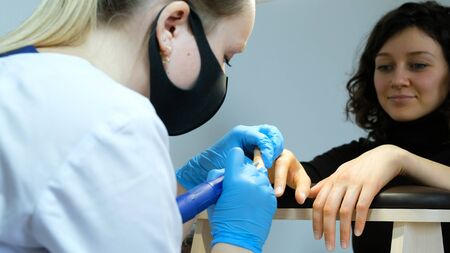 Manicurist, nail artist handles nails with manicure milling cutter. Beauty service, nail salon, health care and cosmetics. Close upの写真素材