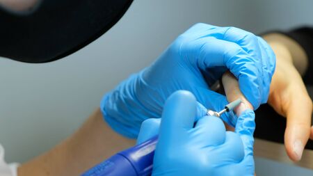 Manicurist, nail artist handles nails with manicure milling cutter. Beauty service, nail salon, health care and cosmetics. Close upの写真素材